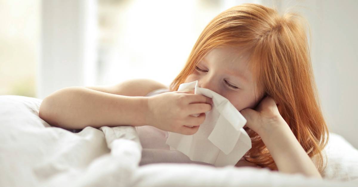 A young girl blowing her nose on a tissue
